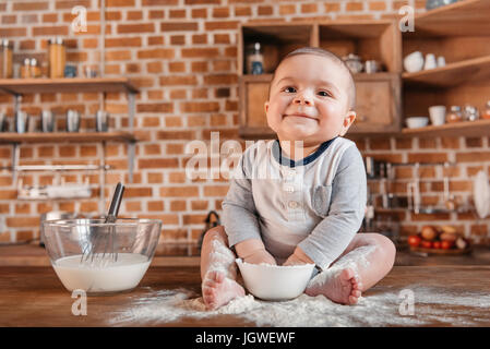 Glückliche kleine Junge spielt mit Mehl und sitzen am Küchentisch. Inländische Lebenskonzept Stockfoto