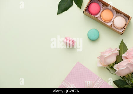 Französische Makronen. Viele süße bunte Macarons in Box mit Blumenstrauß aus Rosen auf dem Tisch Stockfoto
