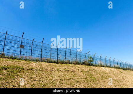 Ein Rahmen mit einer doppelten Draht-Zaun mit Stacheldraht auf einer Bank unter einer sengenden Sonne und blauen Sommerhimmel gemacht. Stockfoto