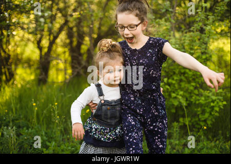 Mädchen und kleine Schwester spielen im Feld mit Bäumen Stockfoto
