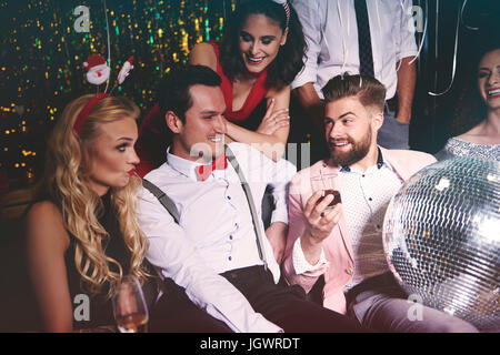 Gruppe von Freunden Zusammensitzen auf Party, Mann, der Disco-Kugel im Schoß hält Stockfoto