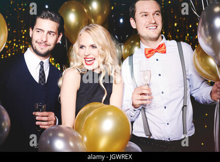 Porträt von drei Personen auf Party, umgeben von Luftballons, hält Champagner Gläser Stockfoto