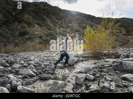 Junge springt über Felsen im Flussbett Stockfoto