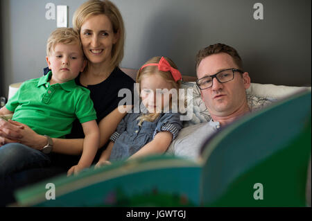 Eltern auf Sofa lesen Märchenbuch, Sohn und Tochter Stockfoto