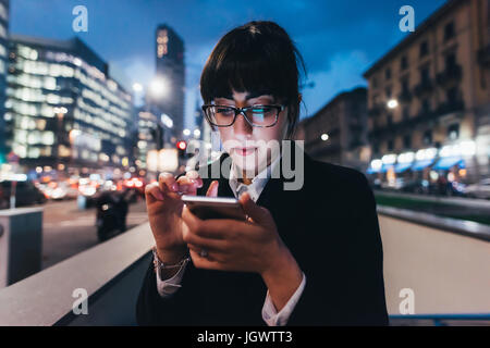 Geschäftsfrau mit Handy von Mauer am viel befahrenen Straße, Mailand, Italien Stockfoto