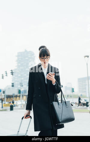 Geschäftsfrau mit mobilen und ziehende Trolley Gepäck, Mailand, Italien Stockfoto