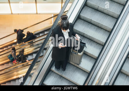 Geschäftsfrau mit Handy auf Rolltreppe, Mailand, Italien Stockfoto