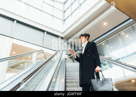 Geschäftsfrau mit Handy auf Rolltreppe, Mailand, Italien Stockfoto
