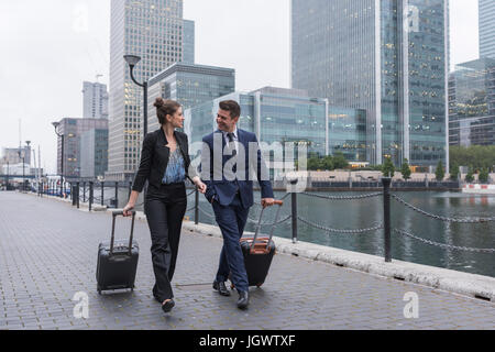 Unternehmer und Unternehmerin ziehen Trolley Gepäck, Canary Wharf, London, UK Stockfoto