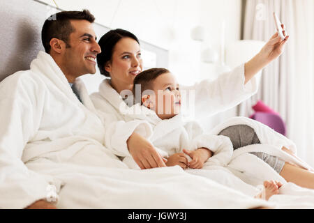 glückliche Familie mit Smartphone im Bett im Hotelzimmer Stockfoto