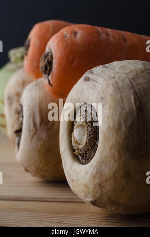 Eine Nahaufnahme der Auswahl von ungewaschenen Wurzelgemüse - Pastinaken; Karotten und Kohlrabi - in einer Reihe führender in Hintergrund auf einem Holz beplankt Küchentisch.  B Stockfoto