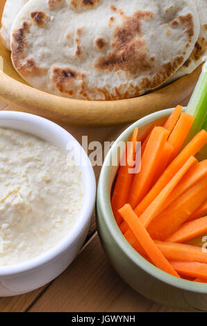 Nahaufnahme der Schalen mit Hummus-Dip; Mini-Pitta-Brot und Karotten und Sellerie Crudites auf einem Holzbrett-Tisch.  Das Diner Perspektive entnommen Stockfoto