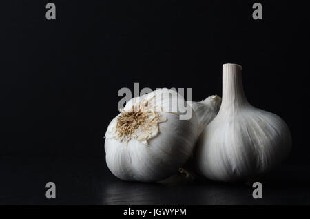 Stillleben-Zusammensetzung der drei ganze Knoblauch Zwiebeln auf schwarzem Schiefer auf schwarzem Hintergrund. Stockfoto