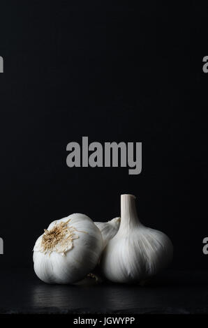 Stillleben-Zusammensetzung der drei ganze Knoblauch Zwiebeln auf schwarzem Schiefer auf schwarzem Hintergrund. Stockfoto