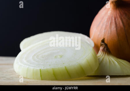 Nahaufnahme von Zwiebel Scheiben auf Holz hacken mit ganze, ungeschälte Zwiebel hinter an Bord und schwarzem Hintergrund. Stockfoto