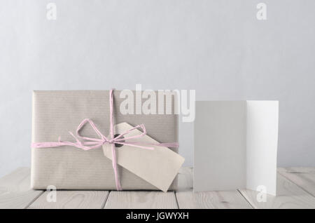 Foto von einer Geschenkbox verpackt in braunem Papier, gebunden an einen Bogen mit mit blass eisigen rosa Bast und leere Tag Paketschein nach vorne.  Daneben Stockfoto