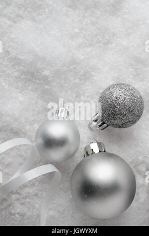 Drei silberne sphärische Christbaumkugeln erschossen overhead auf künstliche Smow mit einem Wirbel von White Ribbon Eisstockschießen. Stockfoto