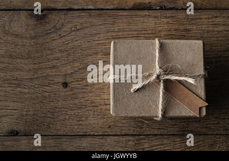 Eine einfache gebunden String Geschenkkasten oder das Paket mit einem leeren Vintage-Stil-Label-Tag.  Auf einer alten Eiche geplankte Holztisch über Kopf gedreht. Stockfoto