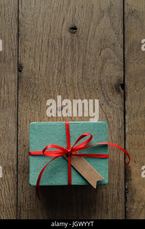 Overhead Schuss von Türkis Geschenk-Box auf einer alten Eiche Holz beplankt Tabelle, gebunden an einen Bogen mit rotem Satinband mit einer leeren Vintage-Stil Nachricht Tag fa Stockfoto