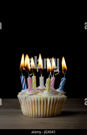 Ein Geburtstag Cupcake bei Normalpapier mit sieben gestreift, brennende Kerzen auf einem Holztisch mit schwarzem Hintergrund. Stockfoto