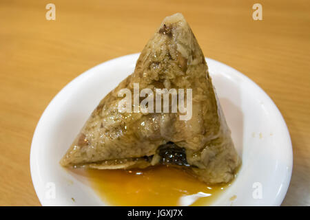 Die Nahaufnahme des chinesischen klebrigen Reisknödlings (Zongzi) auf einem kleinen weißen Teller. Stockfoto