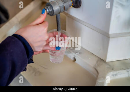 Frau schüttet Mineralwasser im Glas in der Trinkhalle Stockfoto