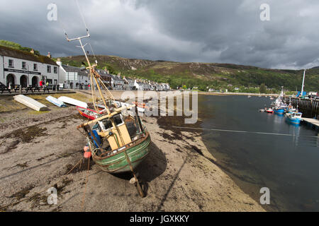 Stadt von Ullapool, Schottland. Ein gestrandeter Fischerboot bei Ebbe mit Shore Street und Ullapool Hafen im Hintergrund. Stockfoto