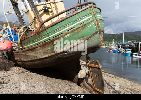 Stadt von Ullapool, Schottland. Malerische Aussicht auf einem gestrandeten Fischerboot bei Ebbe mit Ullapool Hafen im Hintergrund. Stockfoto