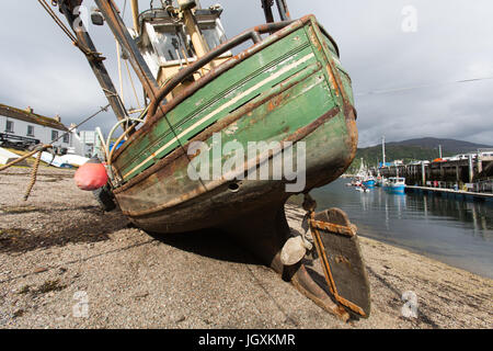 Stadt von Ullapool, Schottland. Malerische Aussicht auf einem gestrandeten Fischerboot bei Ebbe mit Ullapool Hafen im Hintergrund. Stockfoto