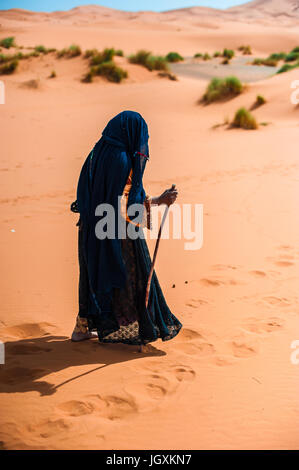 alte Berber Frau allein zu Fuß auf einer Sanddüne in Merzouga, Marokko Stockfoto