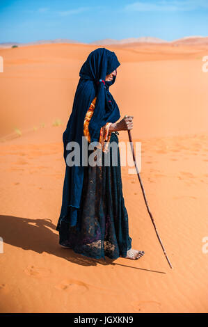 alte Berber Frau allein zu Fuß auf einer Sanddüne in Merzouga, Marokko Stockfoto