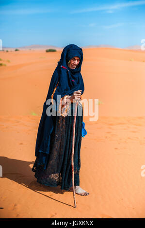 alte Berber Frau allein zu Fuß auf einer Sanddüne in Merzouga, Marokko Stockfoto