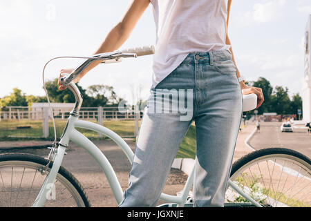 Junge Frau in Jeans und T-shirt mit dem Fahrrad in den Park im Sommer abgeschnitten Bild Stockfoto