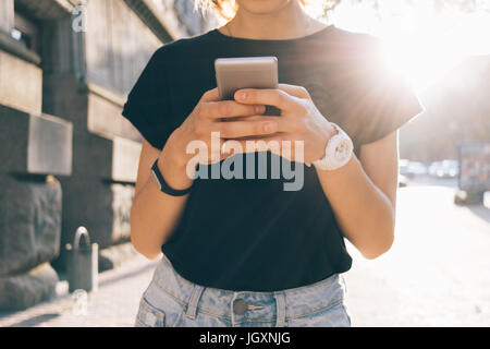 Junge Frau in Jeans und T-shirt mit Gadgets in der Stadt abgeschnitten Bild Stockfoto
