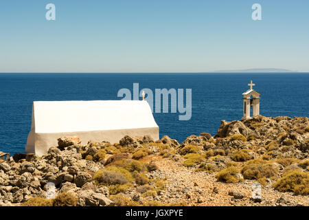 Entfernten, kleinen, weißen griechischen Kirche auf Felsen direkt am Meer an der Südküste von Kreta, Westgriechenland, mit einem separaten Glockenturm gebaut. Stockfoto