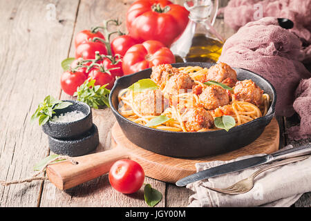 Spaghetti Nudeln mit Fleischbällchen und Tomatensauce in Gusseisen Pfanne bei hölzernen Hintergrund, Nahaufnahme Stockfoto