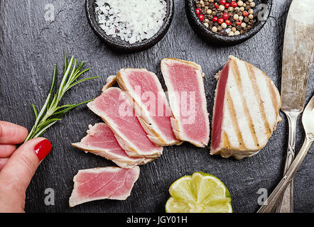 Nahaufnahme von Gebratene gegrillter Thunfisch Steaks auf Schiefer Oberfläche mit Gewürzen und Zitrone, Ansicht von oben Stockfoto