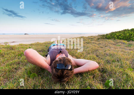 Ein junger Mann tritt zurück und entspannt auf dem Rasen über einen schönen Strand in Australien. Stockfoto