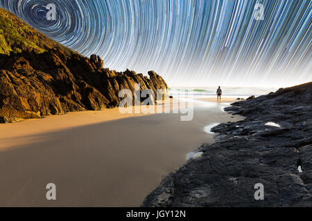 Ein Mann steht auf einem schönen, abgelegenen Strand in Australien unter eine faszinierende Sternspur Stockfoto