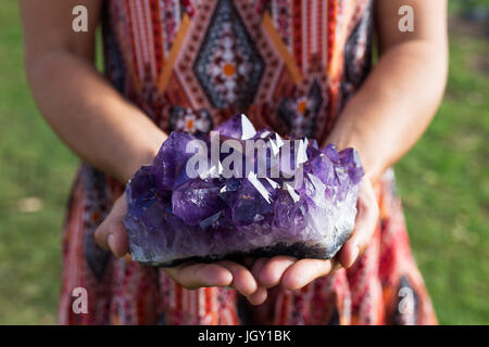 Eine junge Frau hält eine große Ansammlung von Amethyst Kristalle, wie sie im Sonnenlicht schimmern. Stockfoto