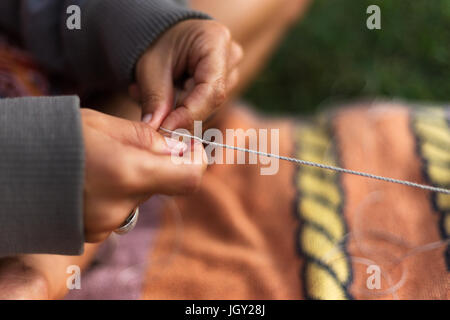 Eine Nahaufnahme von einem Mädchen Händen zart weben Zeichenfolge beim Sitzen mit gekreuzten Beinen auf einem Handtuch im Freien. Stockfoto