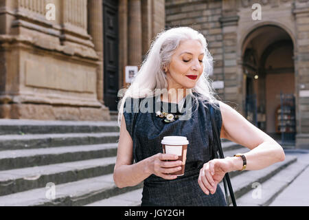 Reife Frau mit langen grauen Haaren betrachten Armbanduhr in Florenz, Italien Stockfoto