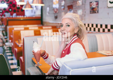 Porträt von Reife Frau in Baseballjacke mit Milchshake im 50er Jahre diner Stockfoto