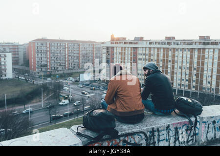 Rückansicht des zwei junge männliche Hipster sitzen an Wand über Stadtbild Stockfoto