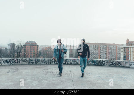 Zwei junge männliche Hipster gehen auf Stadt-Dachterrasse Stockfoto