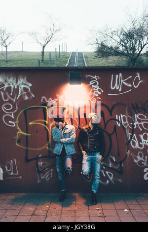 Porträt von zwei coole junge männliche Hipster Graffitiwand gelehnt Stockfoto