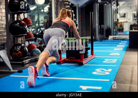 Rückansicht des jungen Frau, training, Turnhalle Gewicht Schlitten einschieben Stockfoto