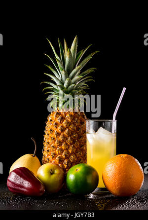 Komposition mit tropischen Früchten und ein Glas Saft auf einem schwarzen reflektierenden Hintergrund mit Wassertropfen, Studio gedreht, Stockfoto