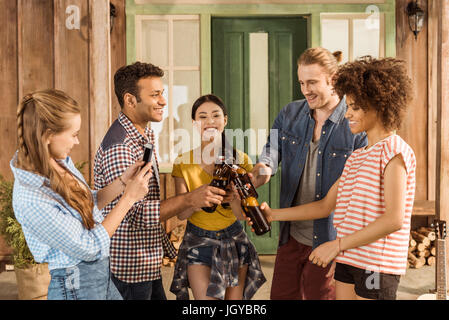 multiethnische Gruppe befreundeter Klirren mit Bier während Mädchen nehmen Foto auf smartphone Stockfoto