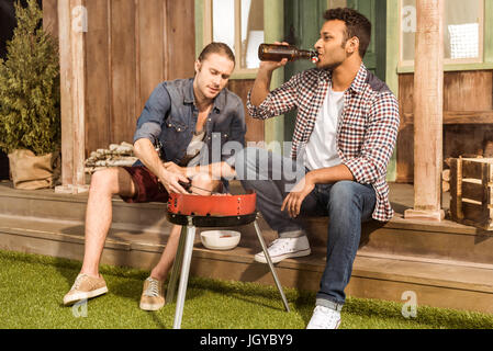 Zwei junge Männer Bier trinken und Zubereitung von Fleisch am Grill im freien Stockfoto